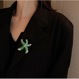 Detailed close-up of emerald green starfish brooch with white crystal flowers on a black suit