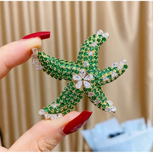 Detailed macro view of starfish brooch featuring green cubic zirconia and gold finish