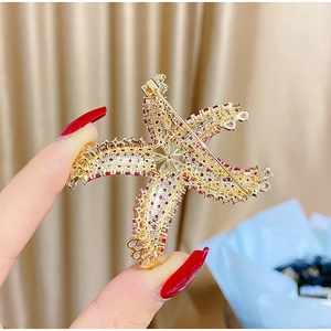Detailed view of starfish brooch featuring red and white zircons on golden plating