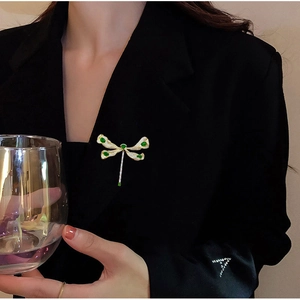 Detailansicht einer eleganten Gold-Libellen-Brosche mit grünen Steinen auf Blazer