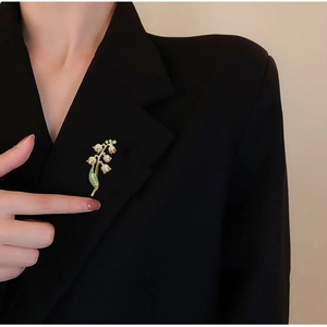Vue détaillée d'une broche muguet avec gemmes vertes sur le revers d'un costume