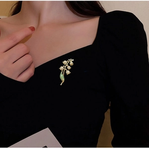 Gros plan d'une broche muguet élégante avec feuilles vertes sur tissu noir