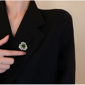 Elegante goldene Blumenbrosche mit grünem Stein am Revers eines schwarzen Blazers