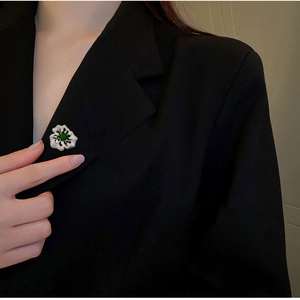 Makroaufnahme einer eleganten grünen Blumenbrosche mit Kristallen auf schwarzem Blazer