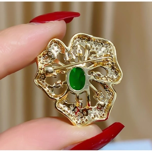 Detailansicht der goldenen Blumenbrosche mit grünem Edelstein und Hohlblättern