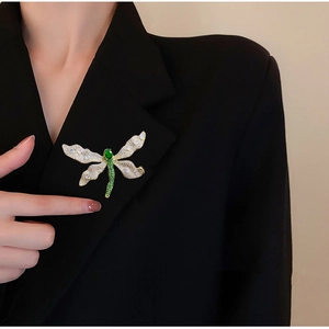 Spilla a libellula con cristalli verdi e bianchi applicata sul bavero di un blazer