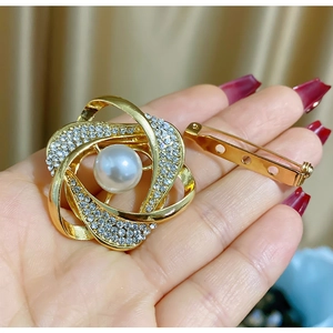 Élégante broche fleur dorée avec perle blanche et cristaux scintillants dans la main