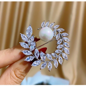 Elegant wheat wreath brooch with white pearls and marquise zircons held by hand