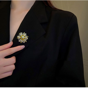 Detail of a rotating snowflake brooch with zircon stones pinned to a black blazer lapel