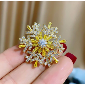 Elegant rotating snowflake brooch with yellow zircons and gold plating held by hand