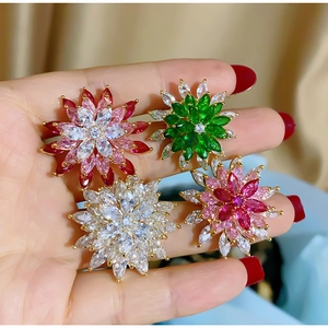 Detailed view of four colorful zircon flower brooches held by hand to show actual size
