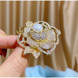 Gros plan sur une broche rose dorée avec pétales en zircone et perle blanche centrale