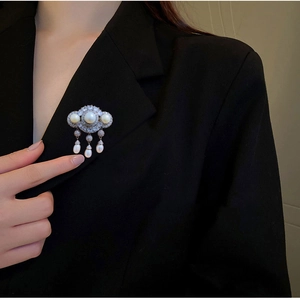 Close-up of elegant tassel brooch with white pearls and sparkling zircons on black blazer