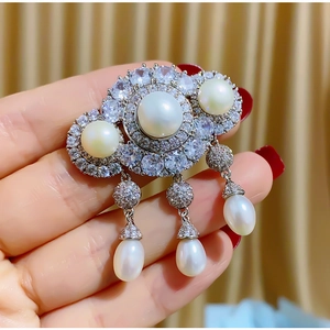 Luxurious silver brooch with white pearls and zircons on golden velvet background