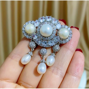 Macro detail of luxury silver brooch with white pearls, zircons and tassel drops