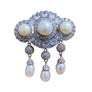 Elegant pearl and rhinestone brooch with dangling tassels and crystals on a white background