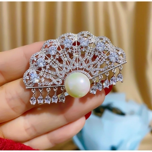 Detail of elegant fan-shaped brooch with zircon stones, pearls and a hanging drop pendant