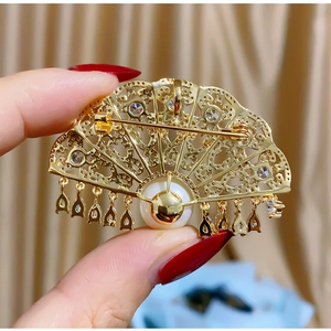 Elegant gold fan-shaped brooch with intricate hollow patterns, rhinestones and pearls