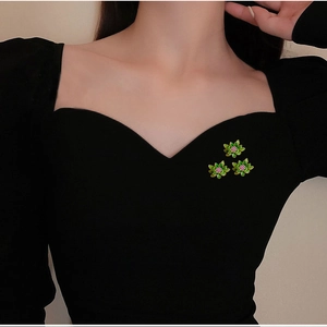 Macro detail of three green lotus flower brooches with pink crystals on black fabric