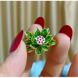 Vintage lotus brooch with green enamel petals and pink gemstones held by a hand