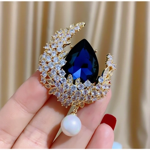 Elegante spilla a mezzaluna dorata con gemma blu a goccia e perla pendente