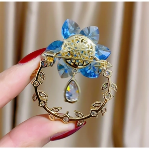 Dettaglio della spilla a fiore con cristalli blu e ciondolo a goccia dorato