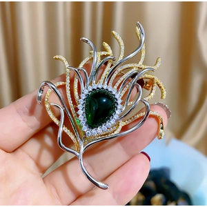 Exaggerated peacock feather brooch with a pear-cut green gemstone and sparkling crystals
