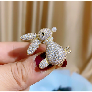 Close-up of golden bunny brooch with micro-pave zircons and small pearls on a warm backdrop
