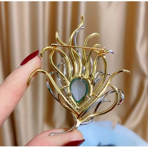 Macro detail of the back structure and safety pin on a gold feather brooch with green gem