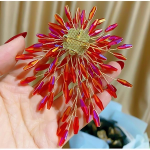 Détail macro d'une broche en perles rouges faite main avec cristaux et fils dorés