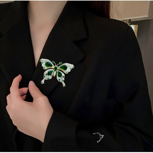 Broche papillon luxueuse avec émeraudes et strass scintillants sur un revers noir