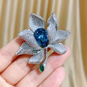 Makroaufnahme einer silbernen Blumenbrosche mit blauem Kristall und Zirkon-Blütenblättern