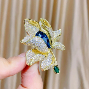 Detailaufnahme einer Blumenbrosche mit blauem Kristalltropfen und Goldblüten-Zirkonia