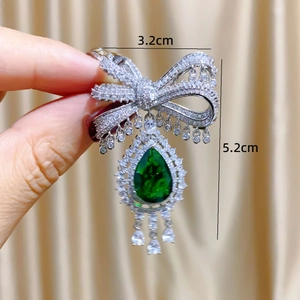 Luxurious silver bow brooch with emerald green teardrop pendant and crystal pavé
