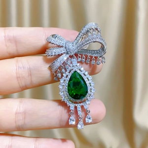 Elegant bow brooch featuring a large pear-cut emerald green gemstone and crystal tassels