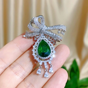 Luxurious bow brooch with large pear-shaped green gemstone and white teardrop pendants