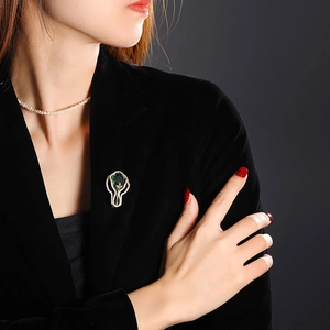 Détail d'une broche vintage vert émeraude avec zircons sur un blazer en velours noir