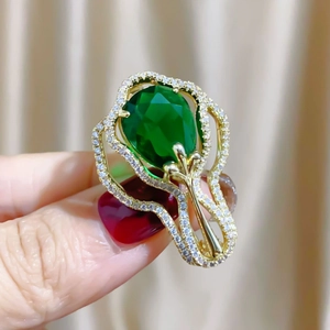 Vue détaillée d'une broche dorée ornée d'une grande pierre verte en forme de poire
