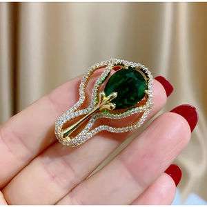 Vue détaillée d'une broche dorée avec gemme verte taille poire et pavage de zircons