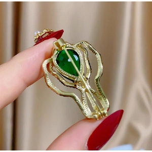 Vue macro d'une broche rétro ajourée avec grand cristal vert poire et placage doré