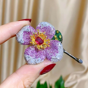 Close-up of luxury flower brooch with pink zircons and green leaves held in hand