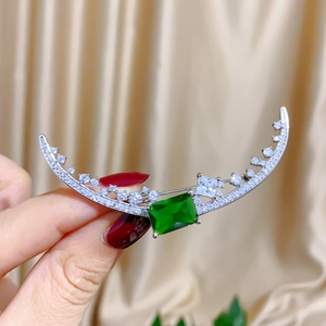 Elegant crescent moon brooch with emerald gemstone and sparkling zircons on silk background