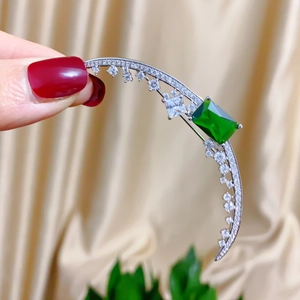 Close-up of crescent moon brooch with green emerald-cut zircon and pave crystals