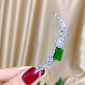 Macro detail of crescent moon brooch with emerald-cut green stone and silver plating