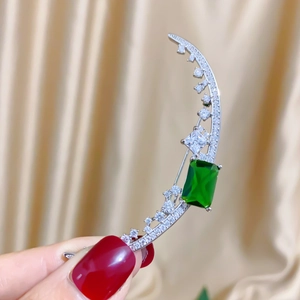 Detailed close-up of crescent moon brooch with micro-pave zircons and green emerald gem