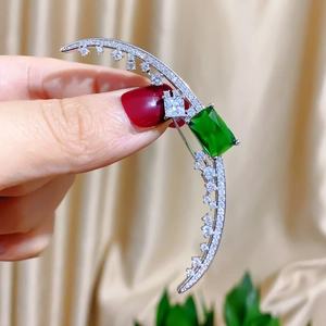 Detail of crescent moon brooch with green gemstone and pavé zircon on silk background