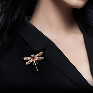 Detailed close-up of a dragonfly brooch with red stones and enamel wings on a black blazer