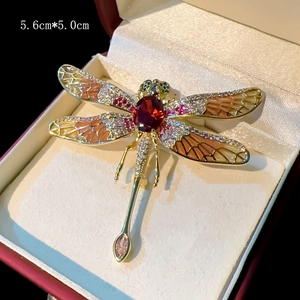Detail of dragonfly brooch with orange enamel wings and red stone on red jewelry box