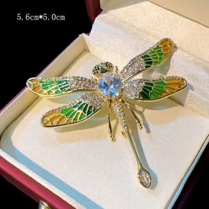 Elegant gold dragonfly brooch with green enamel wings and blue crystals in a gift box