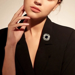 Detailed view of an emerald-cut blue crystal brooch with sunburst zircon halo on a black suit